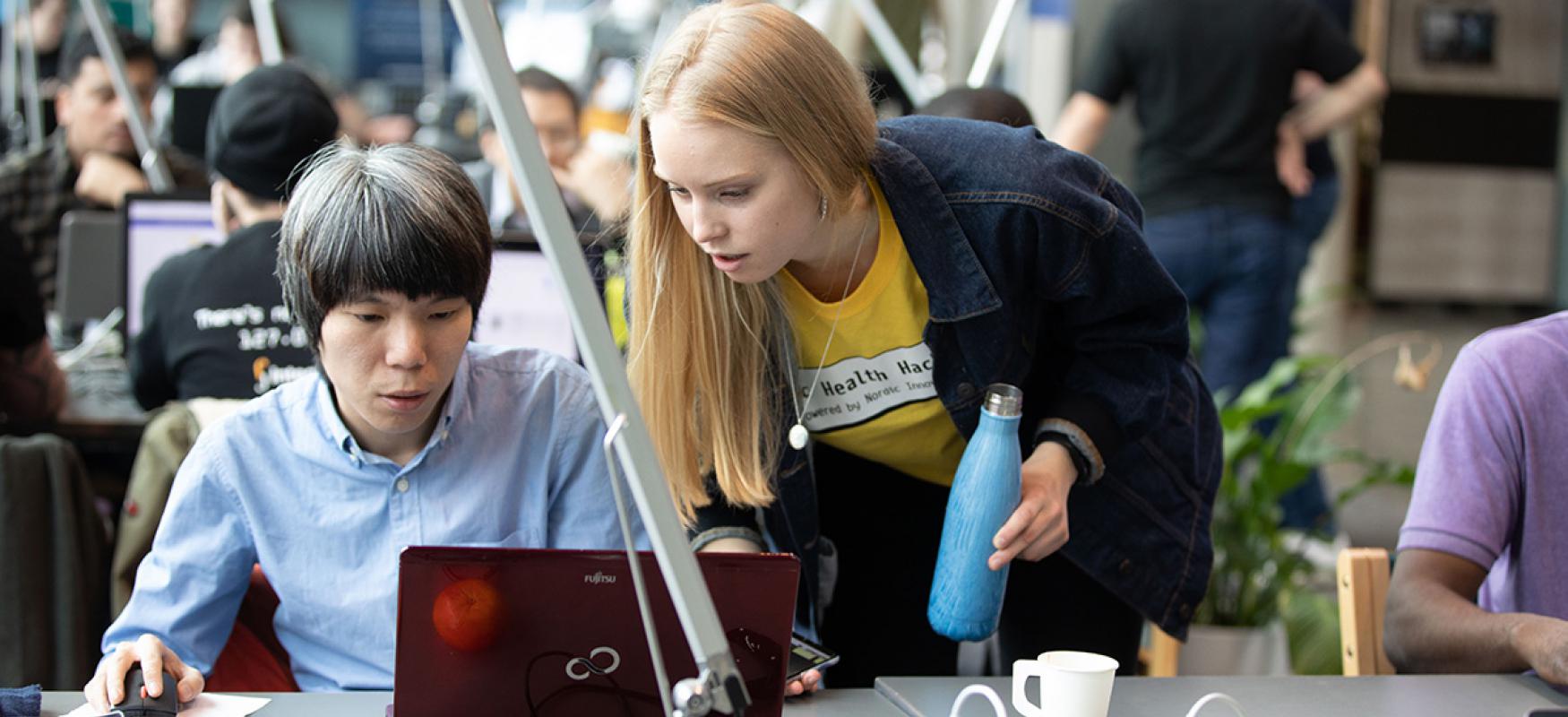 Two people in front of a laptop at a hackathon in Helsinki.