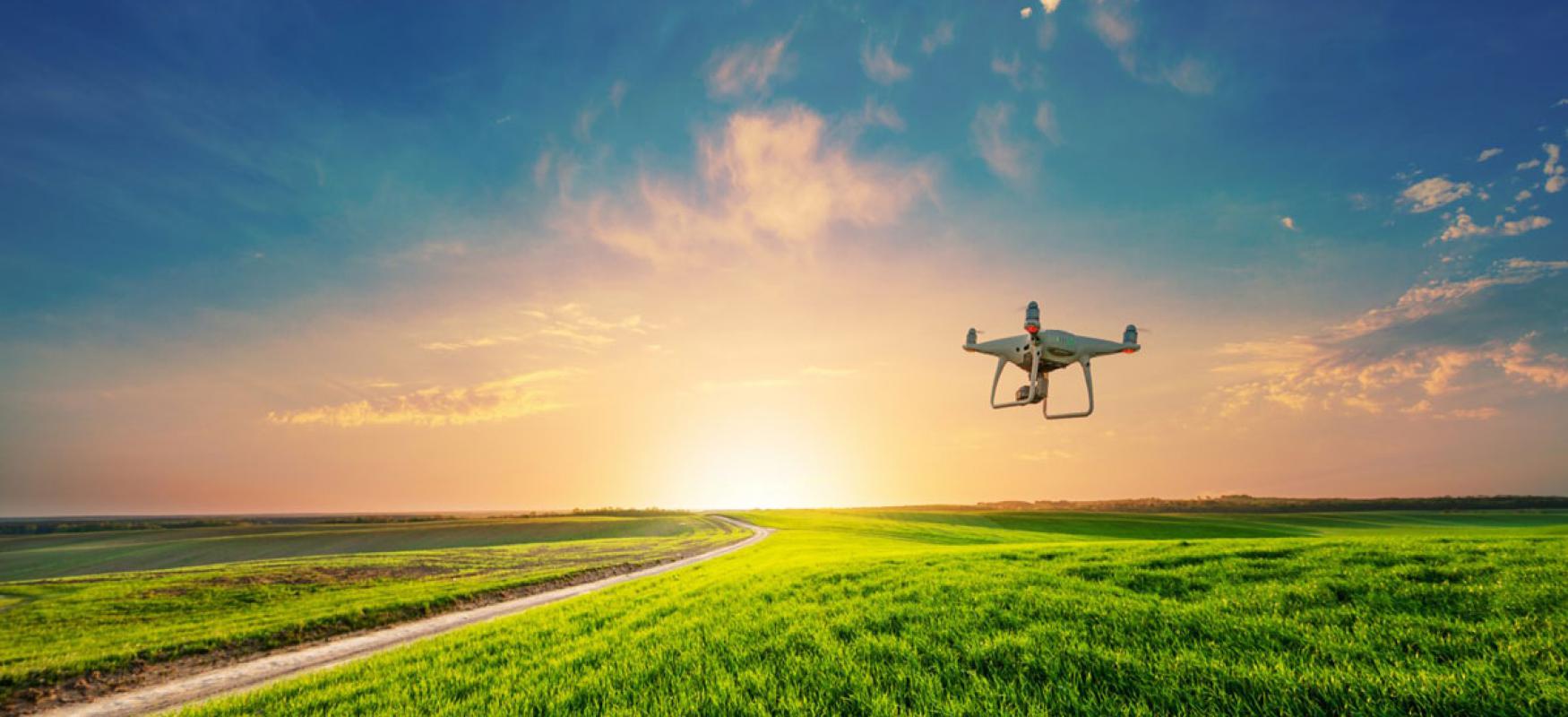 Small drone flying over a green field in the sunset.