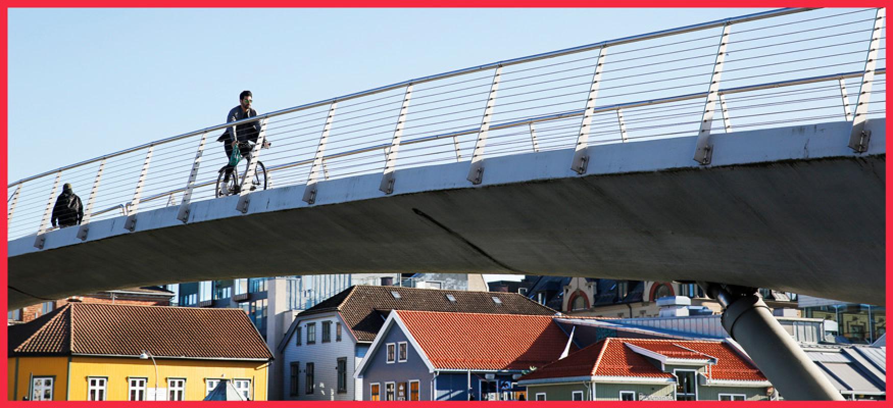 Man cyckling over a bridge with wooden houses in the background