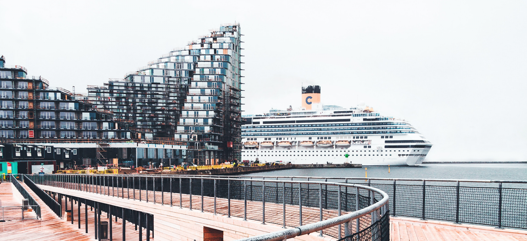 Aarhus Harbor with a cruise ship appearing from behind a large building at the waterfront.