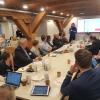 Participants gathered around a large table at a workshop and a person speaking in front of them.