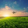 Small drone flying over a green field in the sunset.