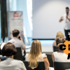 Man standing one stage pitching his idea to a seated audience.